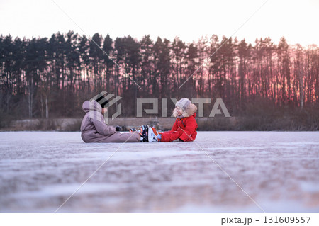 Girls in warm winter overalls relax on the surface of a frozen lake. Ice skating 131609557
