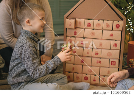 A child opens a box with a surprise Advent calendar surrounded by parents sitting on the floor by a Christmas tree A child opens a box with a surprise Advent calendar surrounded by parents sitting on the floor by a Christmas tree 131609562