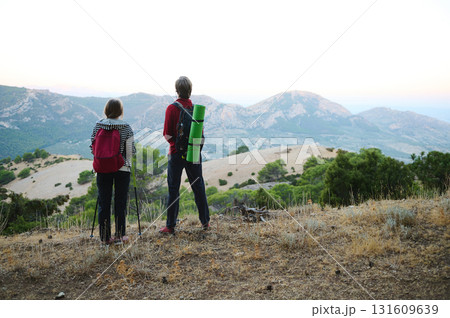 Hikers Standing on Hilltop Overlooking Mountain Range at Dawn Hikers Standing on Hilltop Overlooking Mountain Range at Dawn 131609639