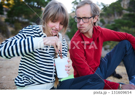 Casual Outdoor Couple Sipping Drink: Woman In Striped Shirt And Man In Red Hoodie Watch In A Natural, Relaxed Setting 131609654