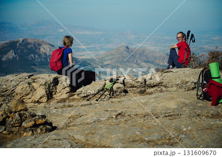 On a Mountain Summit, Friends Hike Together With Backpacks, Trekking Poles, and Dog Beneath Expansive Valley On a Mountain Summit, Friends Hike Together With Backpacks, Trekking Poles, and Dog Beneath Expansive Valley 131609670