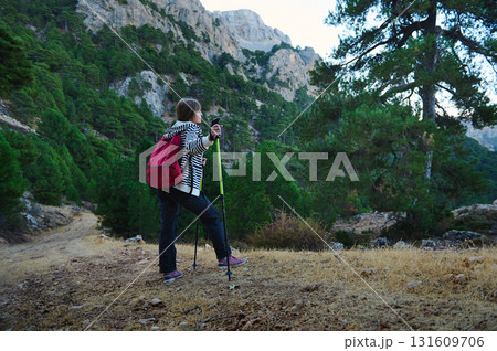 Hiker With Red Backpack Exploring Mountain Trail Among Pines and Rocky Cliffs Hiker With Red Backpack Exploring Mountain Trail Among Pines and Rocky Cliffs 131609706