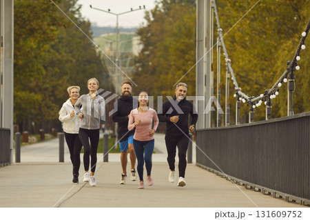 Team of people men and women running together along a bridge in city park. 131609752