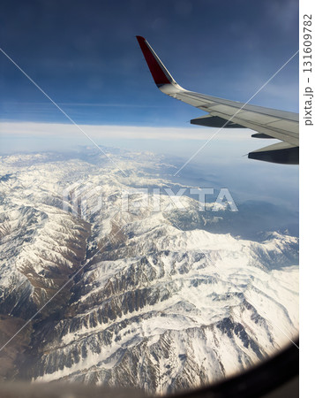 Aerial view of snowy mountain peaks with airplane wing in clear sky 131609782
