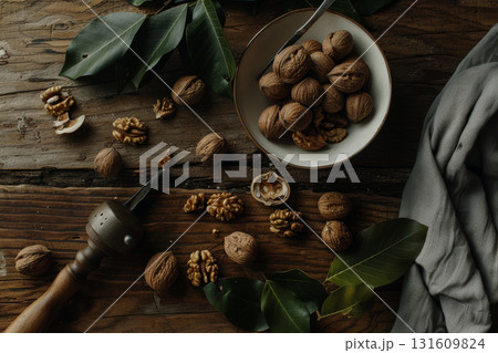 A bowl filled with walnuts sits on a wooden surface, accompanied by green leaves and scattered walnut pieces, creating a natural setting 131609824