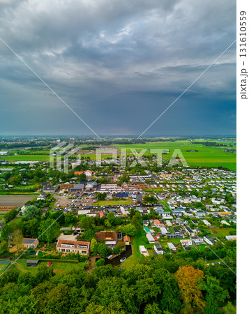 Aerial view of grid pattern residential zone with canal, gardens, and farmland contrasting compact housing with expansive green fields under dramatic overcast skies. 131610559
