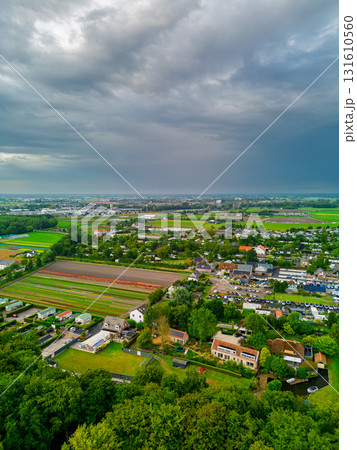 Aerial view of semi rural landscape with tree lined homes, crop fields, and distant town showcasing layered land use under dramatic overcast skies. Aerial view of semi rural landscape with tree lined homes, crop fields, and distant town showcasing layered land use under dramatic overcast skies. 131610560