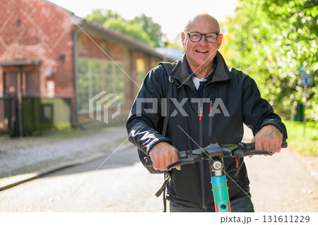 Portrait of a smiling senior man riding a electric kick scooter in city 131611229