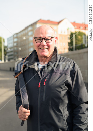 Portrait of a smiling bald senior man with glasses wearing a sport jacket outdoors 131611239