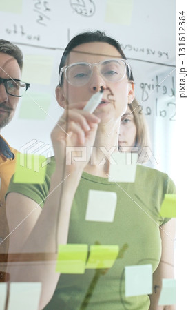 Professional team brainstorming, sharing strategy on glass whiteboard with colorful sticky notes, working collaboratively in bright office space Professional team brainstorming, sharing strategy on glass whiteboard with colorful sticky notes, working collaboratively in bright office space 131612384
