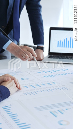 Businessman standing above the table and pointing into financial charts while discussing financial data, market trends during a corporate meeting in office. Business people concept Businessman standing above the table and pointing into financial charts while discussing financial data, market trends during a corporate meeting in office. Business people concept 131612584
