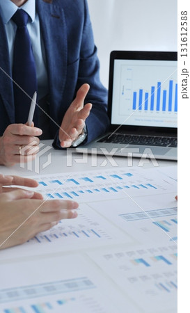 Businesspeople sitting at the table and pointing into financial charts while discussing financial data, market trends during meeting in modern office. Business people concept 131612588