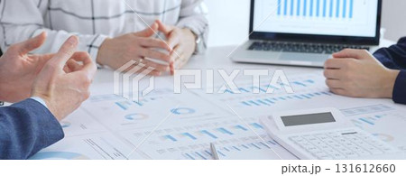 Business professionals discussing financial reports and data analysis during an office meeting, reviewing market trends and performance charts on paper and laptop 131612660