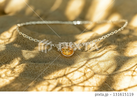 Elegant Silver Necklace with Natural Amber Gemstone Sitting on Golden Sandy Surface Elegant Silver Necklace with Natural Amber Gemstone Sitting on Golden Sandy Surface 131615119