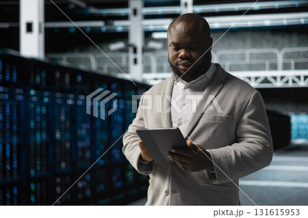 Data center employee fixing network issues affecting rigs performance, scripting automated workflows. Technician running system diagnostic tests, evaluating reports on tablet 131615953