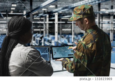 Military server hub personnel analyzing surveillance data together in secure command center. Commander in data center verifying intel accuracy with IT specialist reviewing live tactical feed on screen Military server hub personnel analyzing surveillance data together in secure command center. Commander in data center verifying intel accuracy with IT specialist reviewing live tactical feed on screen 131615969