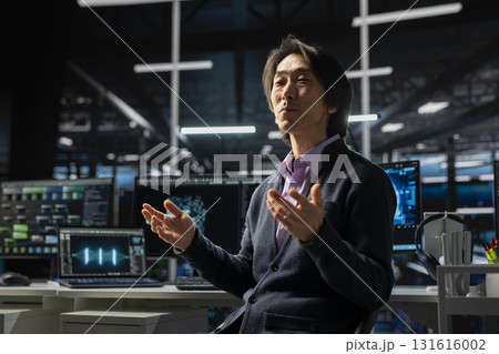 Computer scientist in server room using device to review infrastructure diagnostics. Asian senior programmer in high tech data center analyzing performance data to maintain system uptime Computer scientist in server room using device to review infrastructure diagnostics. Asian senior programmer in high tech data center analyzing performance data to maintain system uptime 131616002