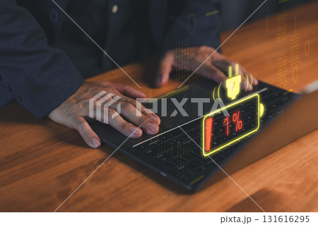Close-up of hands on a laptop computer with a glowing low-battery warning icon at 1%. Concept of technology failure, digital burnout, device charging issues, energy crisis and urgent solutions. 131616295