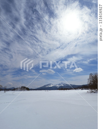 冬の裏磐梯、桧原湖。広大な雪原に立木と冠雪の磐梯山、青空に雲で白く輝く太陽が印象的で綺麗だ。 冬の裏磐梯、桧原湖。広大な雪原に立木と冠雪の磐梯山、青空に雲で白く輝く太陽が印象的で綺麗だ。 131616927