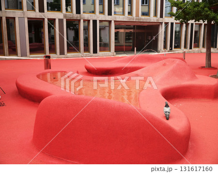 Unique red landscape with pond and art structures in an urban park setting on a sunny day 131617160