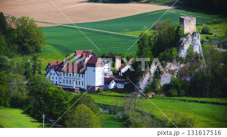 Historic castle overlooks rural landscape with lush fields and quaint buildings during a sunny day in the countryside 131617516