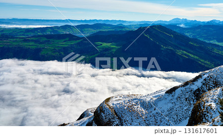 Mountain landscape with snow and clouds during bright daylight near lush green valleys in a serene environment 131617601