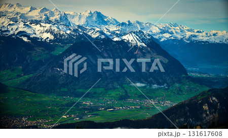 Snow-capped mountains offer stunning views over green valleys and small villages in Switzerland on a clear day Snow-capped mountains offer stunning views over green valleys and small villages in Switzerland on a clear day 131617608