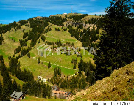 Mountain landscape view showing lush green hills, scattered houses, and a serene sky on a bright sunny day in the Swiss Alps 131617658