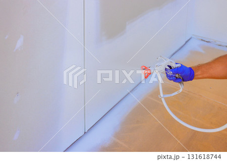 Painter uses spray gun to paint walls in room, showcasing home improvement effort during work day. 131618744