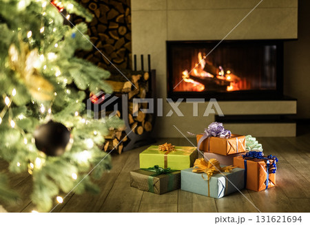 Beautiful Christmas interior with glowing fireplace, decorated tree, and colorful wrapped gifts on the floor, creating a cozy and festive holiday atmosphere at home. 131621694
