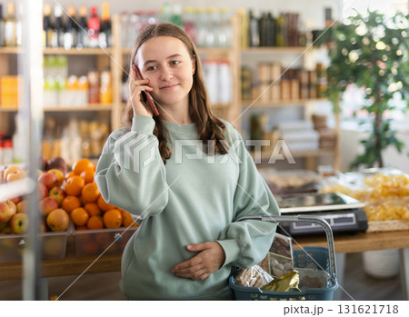 Teenage girl choosing groceries while talking on phone 131621718