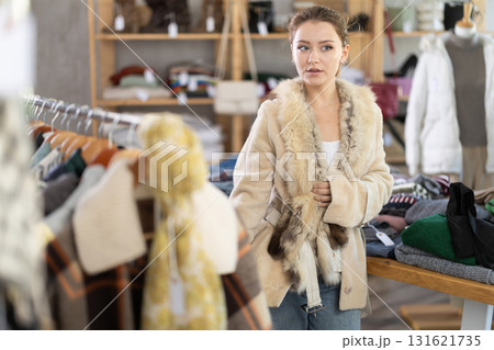 Girl try on fur coat in store and carefully examines her reflection in mirror Girl try on fur coat in store and carefully examines her reflection in mirror 131621735