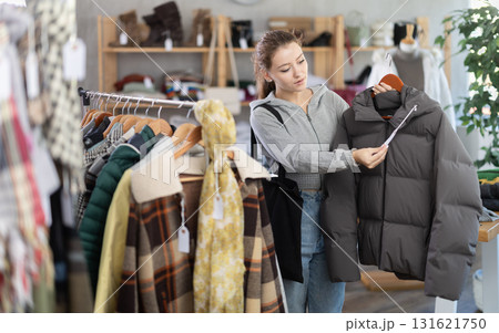 Young woman near showcase examine goods, buying down jacket. 131621750