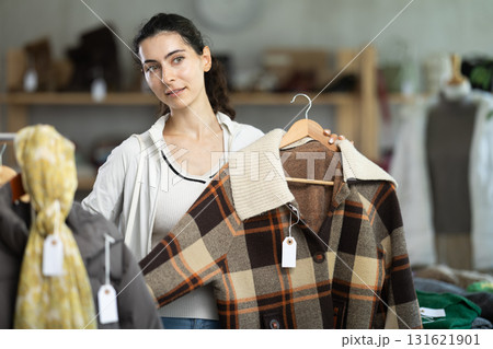 Young woman chooses plaid jacket in clothing store Young woman chooses plaid jacket in clothing store 131621901