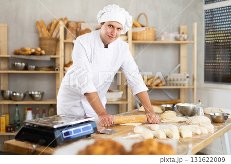 Bakery worker, young baker, rolls out raw yeast dough with rolling pin 131622009