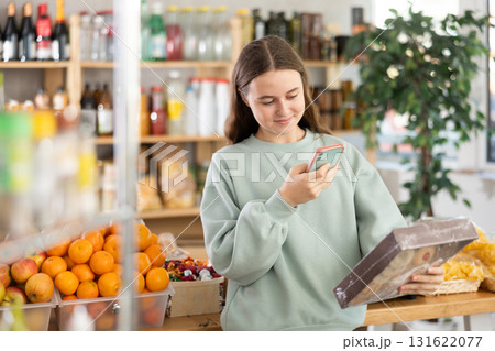 European teen girl customer at shop scans QR code on cookies package using phone camera 131622077