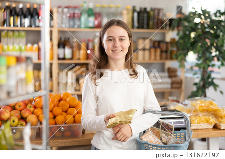Visiting store, teen girl is looking at something on shelf of showcase. 131622197