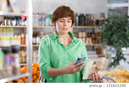 Woman customer holds container with oyster mushrooms in hand, scans QR code on product label 131622200