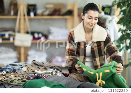 Woman carefully selects a warm sweater, pullover or cardigan in clothing store 131622229