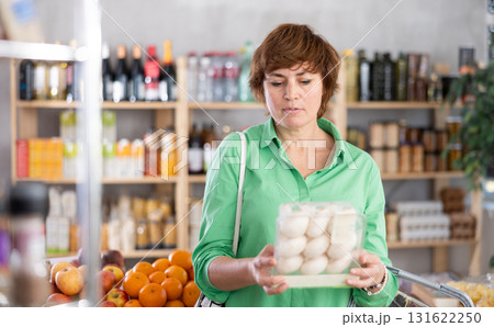 Woman holding plastic containers with champignons, thinking about buying Woman holding plastic containers with champignons, thinking about buying 131622250