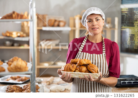 Adult female baker with basket of croissants 131622265