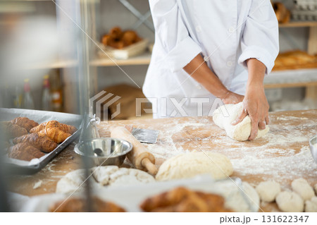 Cute doughs arranged on table in bakery with close-up of female hands skillfully kneading dough at food production line Cute doughs arranged on table in bakery with close-up of female hands skillfully kneading dough at food production line 131622347