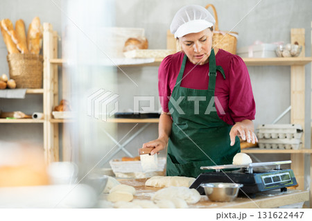 Female cook is working with dough, weighing piece of dough on scale. Female cook is working with dough, weighing piece of dough on scale. 131622447