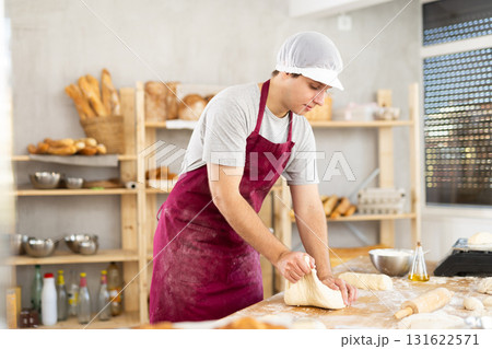 Portrait of young guy baker in apron working with dough, kneading and forming bakery products in kitchen in bakery 131622571