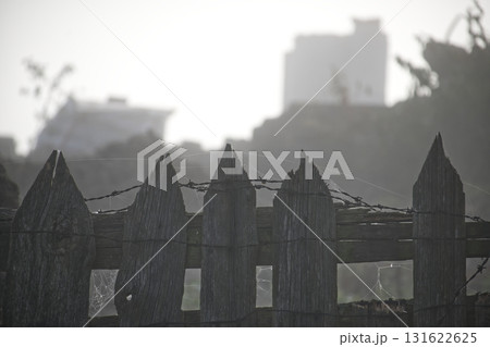 Rustic Wooden Fence With Barbed Wire And Spider Webs Against A Hazy City Background 131622625