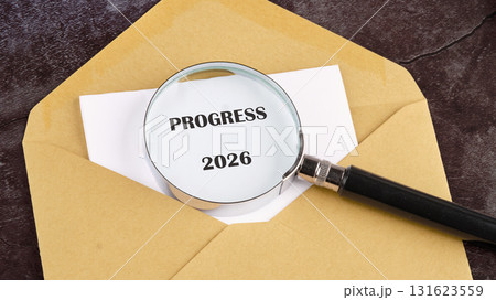 A tan envelope is slightly open. Inside, white paper displays the word PROGRESS and the year 2026. A magnifying glass hovers over it, emphasizing the message A tan envelope is slightly open. Inside, white paper displays the word PROGRESS and the year 2026. A magnifying glass hovers over it, emphasizing the message 131623559