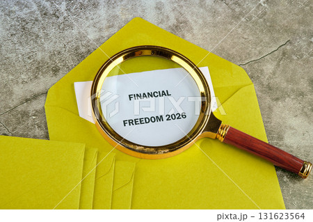 A magnifying glass sits over a yellow envelope, highlighting the words Financial Freedom 2026 written on a piece of paper inside. The background is textured 131623564