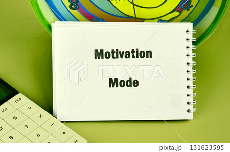 A spiral notebook displays the words Motivation Mode next to a calculator and colorful round object, all set on a solid green background A spiral notebook displays the words Motivation Mode next to a calculator and colorful round object, all set on a solid green background 131623595