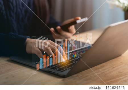 Close-up woman hand engaged in data analysis using a laptop and smartphone in a contemporary workspace, featuring charts and graphs for business insights. 131624243