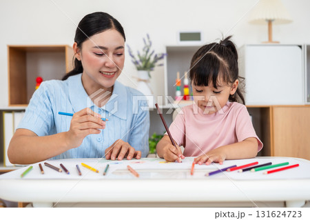 toddler baby girl training to drawing with colored pencil with mother helping on desk at home 131624723